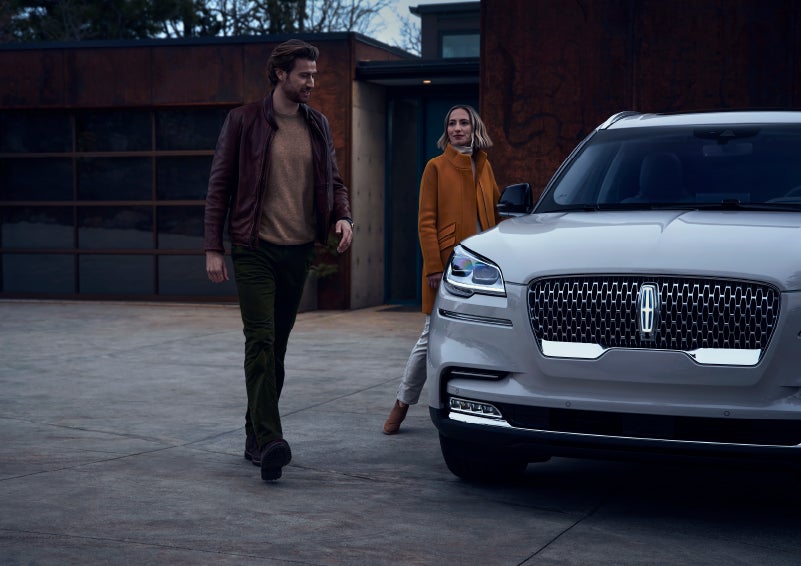 A man and a woman approaching a 2024 Lincoln Aviator® SUV, which illuminates certain lights when they are close | Libertyville Lincoln Sales, Inc. in Libertyville IL
